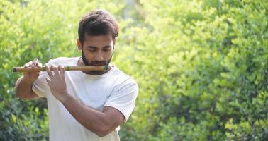 musicista indiano maschio che suona il bansuri con una maglietta bianca. tiro all'aperto su sfondo verde foto