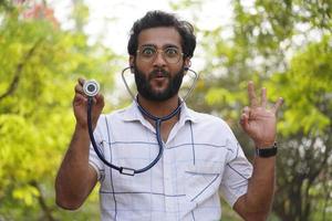 uno studente uscito che mostra lo stetoscopio-studente universitario con lo stetoscopio e che mostra il concetto di educazione medica del segno di successo foto