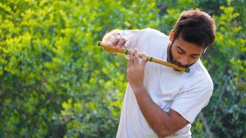 concetto di musica, passione e hobby. musicista indiano maschio che suona il flauto con una maglietta bianca. tiro all'aperto su sfondo verde foto