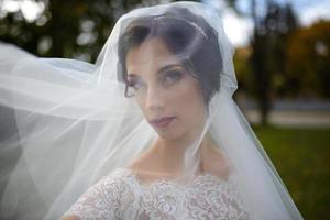 ritratto di una sposa solitaria sullo sfondo di un parco autunnale. la fanciulla si rifugiò sotto un velo con cui si sviluppa il vento. foto