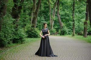 giovane bella donna che posa in un vestito nero in un parco. foto
