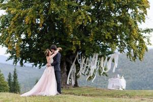 gli sposi si abbracciano sotto una vecchia quercia. servizio fotografico di matrimonio in montagna. foto