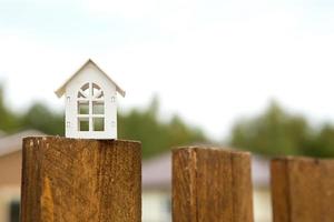 piccola figura di casa in legno bianco sul recinto con chiave per alloggi sullo sfondo dei cottage. costruzione, progettazione, progetto, trasloco in nuova casa, mutuo, affitto e acquisto di immobili. copia spazio foto