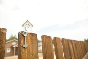 piccola figura di casa in legno bianco sul recinto con chiave per alloggi sullo sfondo dei cottage. costruzione, progettazione, progetto, trasloco in nuova casa, mutuo, affitto e acquisto di immobili. copia spazio foto