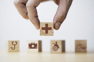 mano che tiene la schermata di stampa delle icone mediche e sanitarie su blocco di legno per un sano concetto di assicurazione e assicurazione per il benessere. foto