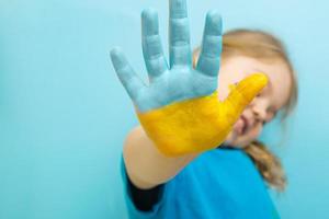 vernice gialla e blu sulla mano di una bambina. concetto di simboli della bandiera ucraina foto