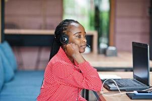 donna afroamericana lavora in un operatore di call center e agente del servizio clienti che indossa cuffie con microfono che lavorano su laptop. foto