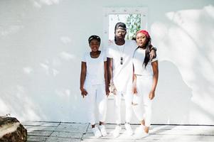 tre eleganti amici afroamericani, indossano abiti bianchi contro lo specchio sul muro. moda di strada dei giovani neri. uomo di colore con due ragazze africane. foto