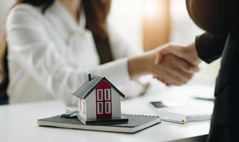 operaio edile che stringe la mano al cliente dopo aver terminato la riunione di lavoro per avviare un contratto di progetto nel centro degli uffici al cantiere dietro il modello di casa, concetto di contratto di mutuo per la casa foto