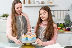 felice madre e figlia che preparano e decorano la torta fatta in casa in cucina. mamma che insegna alla bambina che cuoce la panetteria. attività familiare a casa foto