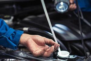 primo piano meccanico a mano che controlla il livello dell'olio nel motore dell'auto. dopo il concetto di servizio di riparazione foto