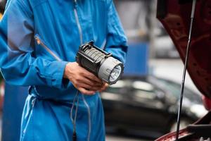 torcia elettrica della tenuta del meccanico che si prepara a riparare il veicolo nel garage dell'auto. dopo attività di servizio, manutenzione automobilistica foto