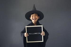 simpatico ragazzo asiatico che celebra halloween indossando un costume da strega e tenendo in mano accessori per la decorazione di halloween foto