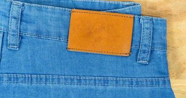 pelle brillante vuota sul retro dei jeans blu, etichetta marrone sulla cintura dei jeans per indossare lettere, sfondi in denim etichetta vestiti in vendita, etichette etichetta pantaloni nuovi di zecca, foto