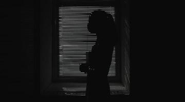 sagoma della ragazza di un medico mascherato contro una finestra con persiane foto