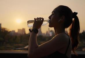 acqua potabile della giovane donna dopo aver fatto jogging al tramonto. foto