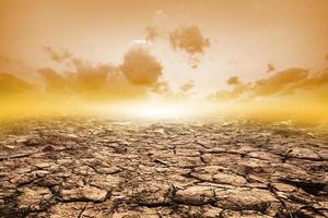 terreno screpolato in estate con il tramonto o crepe del terreno secco nella stagione arida sullo sfondo del cielo arancione. riscaldamento globale foto