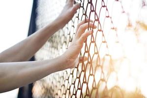 mani di donna che toccano un filo di recinzione metallica foto