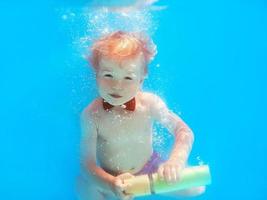bambino piccolo con farfalla rossa che si tuffa sott'acqua in piscina, impara a nuotare. concetto di sport e vacanza foto