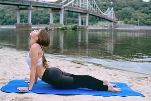 giovane donna in forma in abbigliamento sportivo in diverse asana yoga all'aperto sulla spiaggia vicino al fiume. concetto di yoga e sport foto