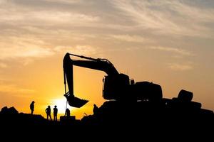 sagoma di caposquadra e squadra di lavoratori in cantiere, operaio edile stradale ed escavatore con sfondo sfocato del tramonto