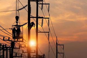 Elettricista silhouette su palo elettrico con sfondo sfocato del cielo al tramonto, squadra di elettricisti silhouette che lavora su pali per installare apparecchiature ad alta tensione