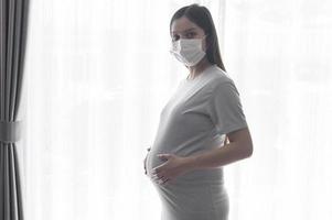 giovane donna incinta che indossa una maschera protettiva e si aspetta un concetto di bambino, sano e maternità foto