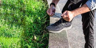 un uomo indossa jeans che si allacciano i lacci delle scarpe nere alla luce del sole in una giornata di sole nel parco. messa a fuoco selettiva, primo piano, spazio di copia, sfondo sfocato foto