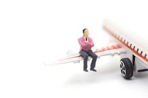 uomo d'affari in miniatura seduto sull'ala dell'aeroplano su sfondo bianco foto