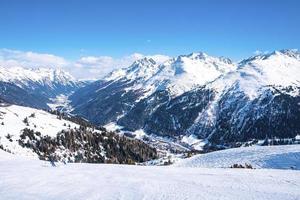 idilliache montagne innevate con fitta foresta contro il cielo nelle alpi foto