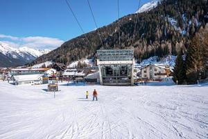 sciatori che sciano verso la stazione sulla montagna innevata nelle alpi con una fitta foresta foto