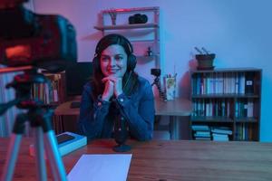bella donna ispanica davanti a una videocamera che registra un blog nel suo studio con luci rosse e blu dentro casa sua foto