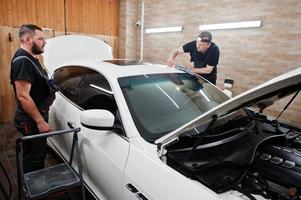 l'operaio nei dettagli il garage ha messo la copertura in pellicola anti-ghiaia in poliuretano in un'auto di lusso bianca. foto