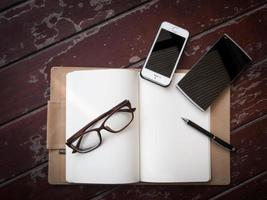 area di lavoro con occhiali, penna e smartphone, carta per appunti e taccuino sul vecchio tavolo di legno foto