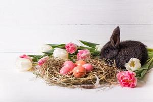 coniglietto pasquale con uova di pasqua con tulipani e un nido di fieno. composizione positiva di primavera e Pasqua. foto