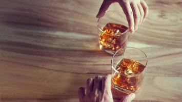 mani di whisky bourbon in due bicchieri su uno sfondo di legno grunge foto