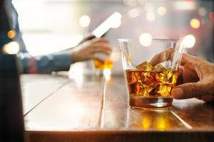 primo piano di due uomini di whisky che bevono bevande alcoliche al bancone del bar sullo sfondo del pub. foto