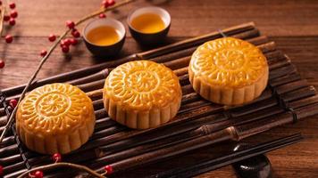 torta di luna di pasticceria tradizionale cinese mooncake con tazze da tè su vassoio di avviso di bambù su sfondo di legno per il festival di metà autunno, primo piano. foto