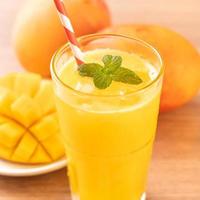 succo di mango fresco con bella polpa di polpa tritata e paglia su sfondo luminoso tavolo in legno. concetto di design di frutta tropicale. primo piano, copia spazio. foto