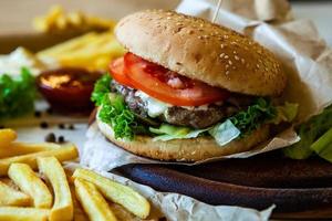 grande hamburger gustoso su un tavolo di legno e patatine fritte. delizioso hamburger con manzo, pomodoro, formaggio e lattuga. foto