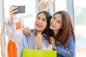 le ragazze asiatiche con l'amico felice godono insieme del selfie divertente del momento di felicità dello shopping nel negozio. foto