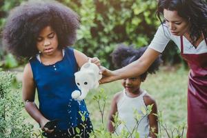 famiglia adorabile giardinaggio irrigazione attività di piante verdi con i bambini durante la permanenza a casa per ridurre lo scoppio del coronavirus. bambini che innaffiano la pianta nel cortile di casa. foto