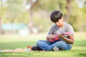 un ragazzo per metà indiano si rilassa imparando a suonare le corde dell'ukulele mentre impara fuori dalla scuola in un parco foto