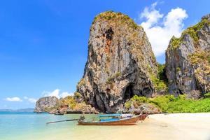 barca a coda lunga e acqua di mare cristallina turchese con scogliera calcarea e montagna sulla spiaggia di phra nang, krabi, tailandia foto