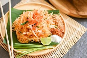 cibo tailandese noodle fritti in stile tailandese con gamberi germogli di soia e guarnizione arachidi peperoncino zucchero in polvere limone lime, pad di noodle saltati in padella tailandese su piatto servito sul tavolo da pranzo cibo foto