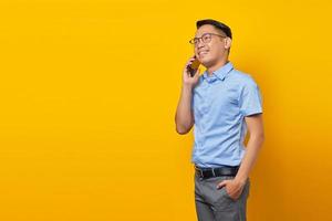 sorridente giovane asiatico asiatico con gli occhiali parlando sul cellulare e guardando da parte isolato su sfondo giallo. concetto di uomo d'affari e imprenditore foto