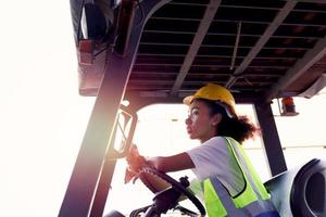 donna operaia industriale che indossa giubbotto di sicurezza e casco guida carrello elevatore auto presso l'industria di fabbrica, ingegnere afroamericano bella donna che lavora al cantiere logistico container cargo. foto