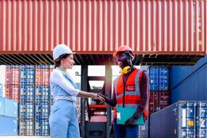 due lavoratori che indossano un casco di sicurezza che si stringono la mano al cantiere di container per carichi logistici. uomo di ingegnere afroamericano che ha una baracca a mano con il suo capo di bella giovane donna dopo una discussione di lavoro foto