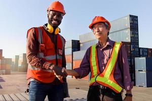 lavoratore che indossa un casco di sicurezza che stringe la mano al cantiere logistico di container per carichi di spedizione. uomo di ingegnere afroamericano che ha una baracca a mano con un ingegnere asiatico anziano anziano dopo la discussione di lavoro foto