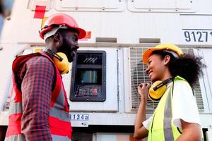 due felici sorridenti industriali afroamericani lavoratore ingegnere uomo e donna indossano giubbotto di sicurezza e casco, lavorano vicino al pulsante del quadro strumenti presso la fabbrica di produzione o il cantiere di spedizione logistico. foto